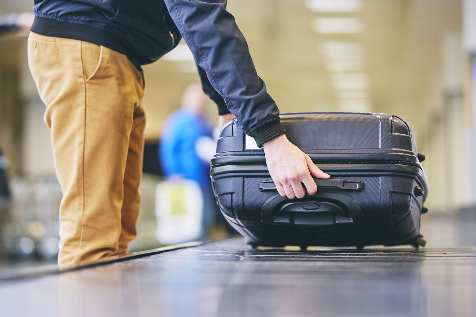 Traveler picking up suitcase from baggage claim in airport terminal.